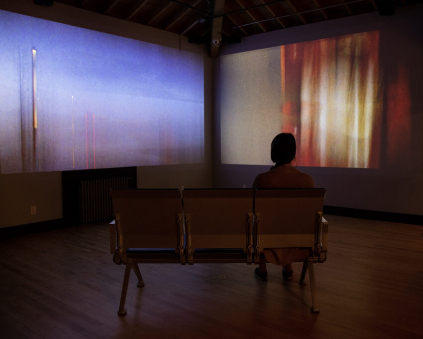 A person sitting on a bench watching two films being projected in a dark room.