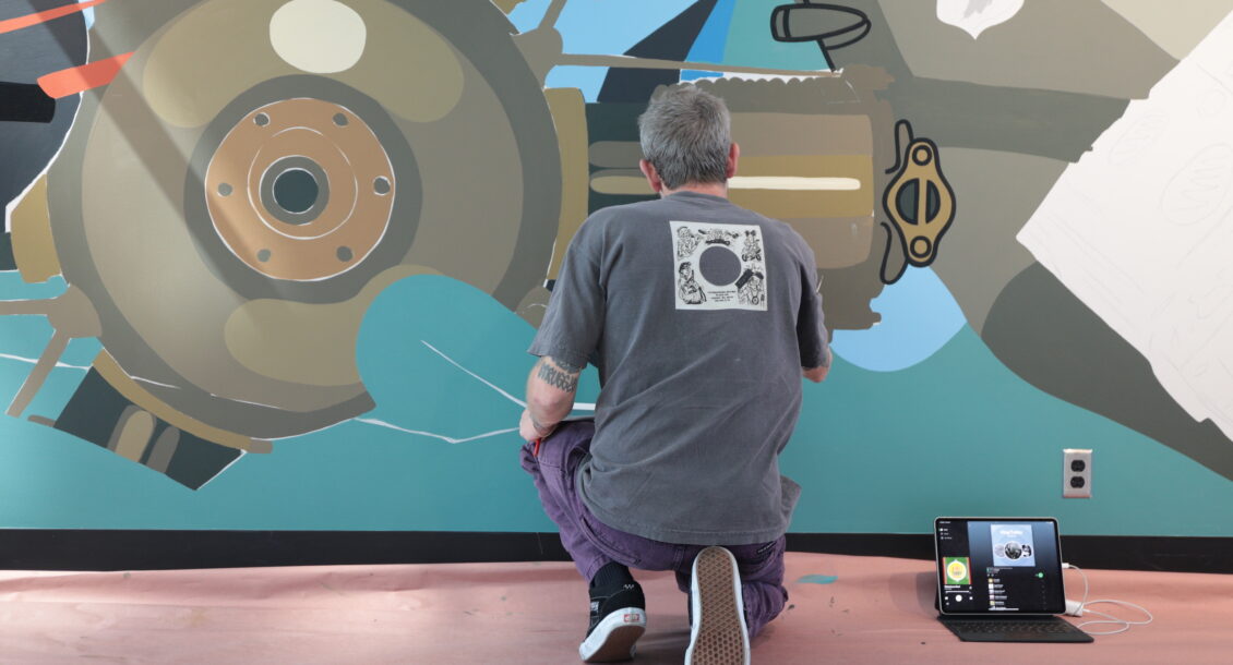 A person kneeling while painting a mural on a wall.