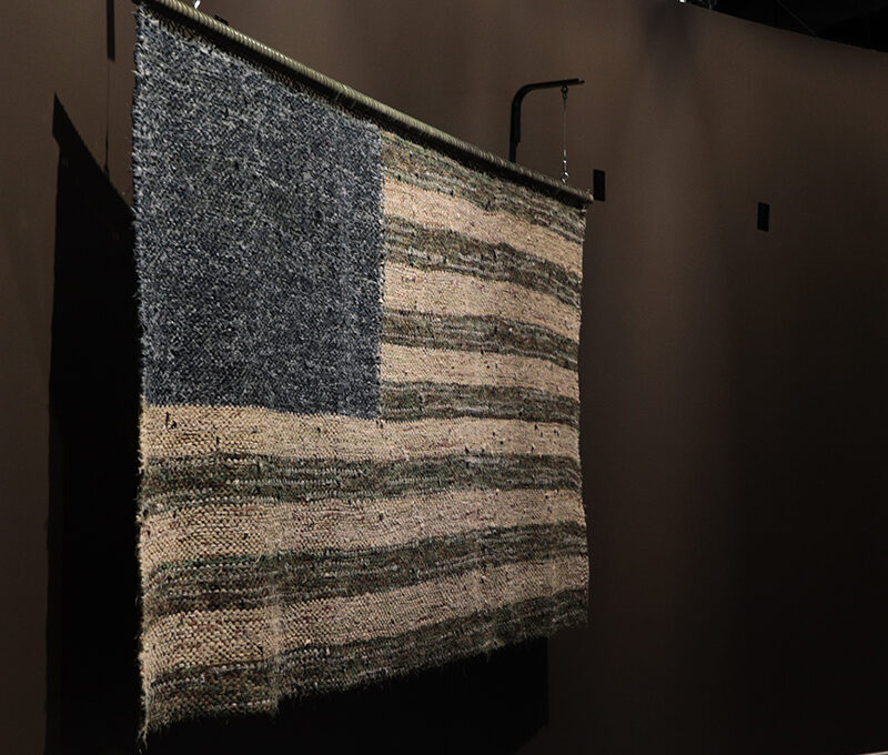 A blue, green, and khaki American flag woven from the uniforms of military service members.