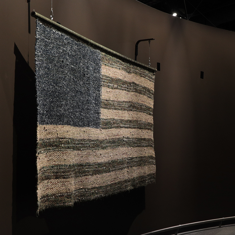 A blue, green, and khaki American flag woven from the uniforms of military service members.