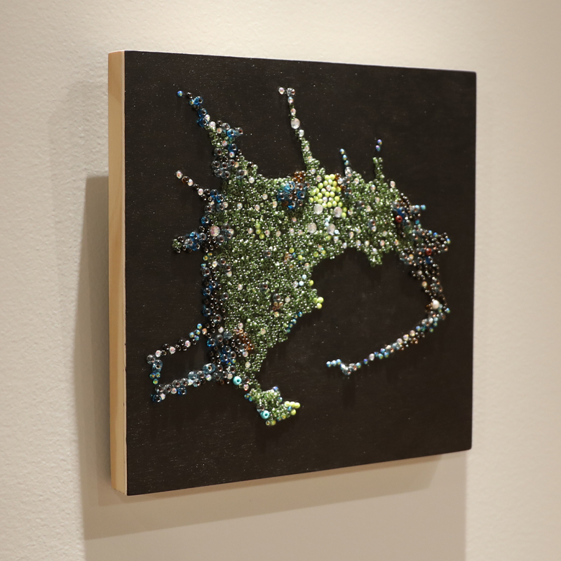 A 2D wood block with green, white and blue beads on a black square panel in the shape of the city of Tokyo.