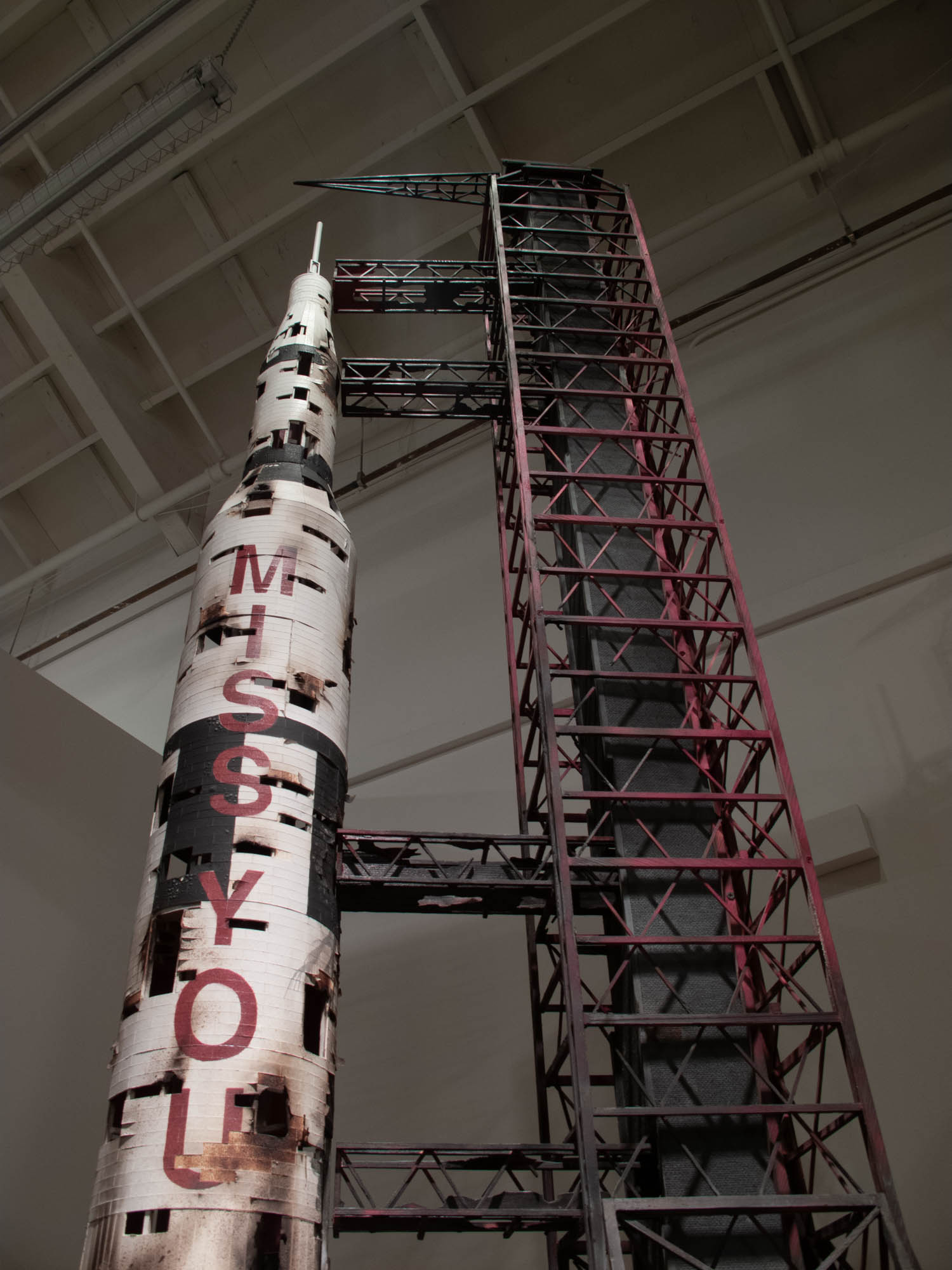 Close-up view of a Saturn V rocket model with burned edges with the words Miss You in bold red.