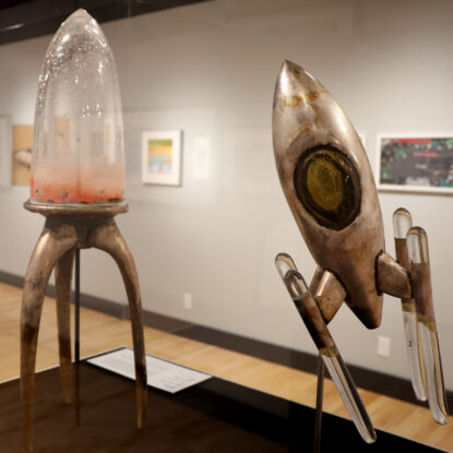 Two mixed media glass sculptures of spaceships in an art gallery.