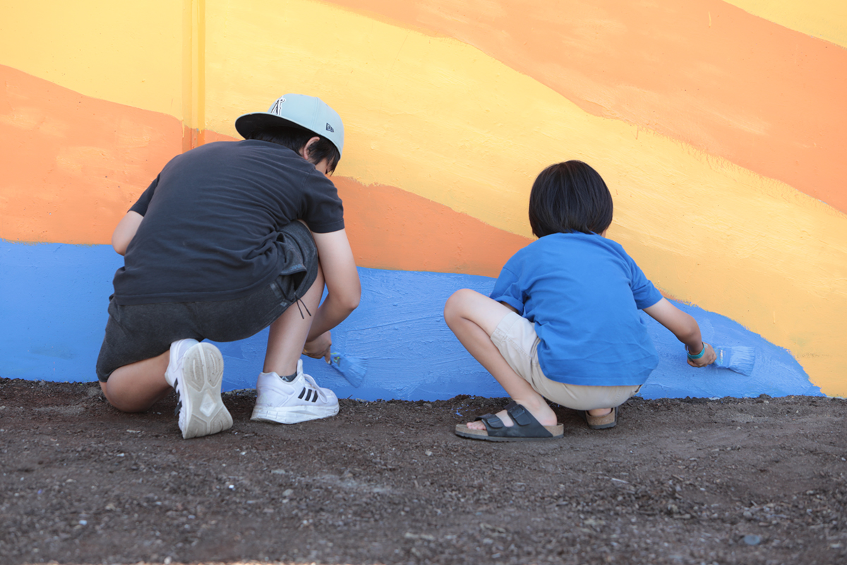 Two little kids paint a lower section of a wall in blue paint.