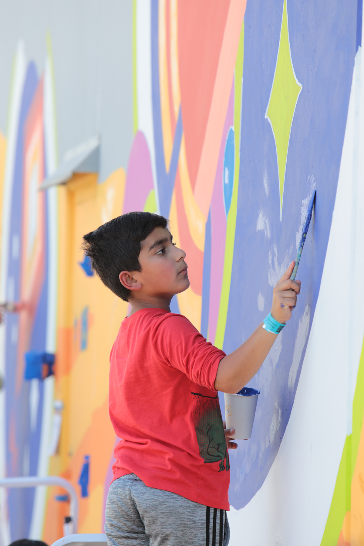 A young teen paints a portion of a wall mural.