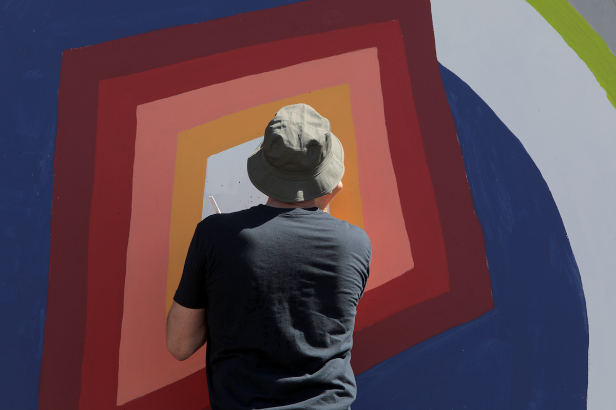 Close-up of a person painting a kite on a wall.
